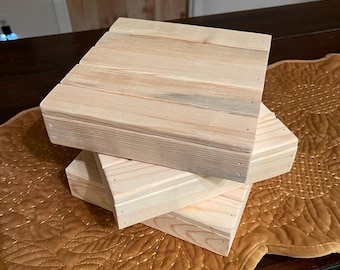 May include: Three wooden square blocks stacked on top of each other. The blocks are made of light wood and have a natural finish. The blocks are sitting on a brown quilted fabric surface.