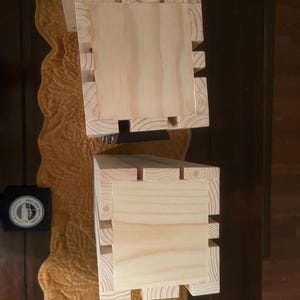 May include: Two unfinished wooden boxes with a natural wood grain. The boxes are rectangular with a square top and a slotted design on the sides. The boxes are likely for storage or display.
