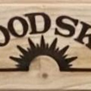 May include: A wooden sign with the words "GOOD SKY" in a dark brown, arched font. Below the text is a stylized sun design. The sign is made of light-colored wood with visible grain.