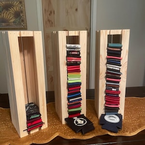 May include: Three wooden display stands filled with colorful beverage can coolers. The stands are made of light-colored wood and are rectangular with vertical slats. The coolers are stacked inside, showcasing a variety of colors and designs.