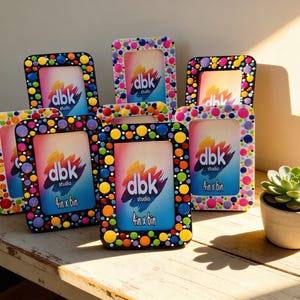 May include: A collection of colorful, hand-painted picture frames. Each frame is decorated with vibrant polka dots in various colors. The frames display the text "dbk studio" and "4in x 6in". A small succulent plant in a white pot sits nearby.