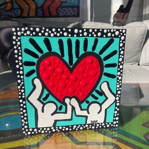 K&ouml;nnte beinhalten: Eine handbemalte Leinwand aus Holz mit t&uuml;rkisfarbenem Hintergrund und wei&szlig;en Punkten. Zwei wei&szlig;e Figuren halten ein gro&szlig;es rotes Herz mit wei&szlig;en Punkten hoch. Das Herz hat schwarze Strahlen, die von ihm ausgehen. Die Leinwand ist unten rechts mit "DBK" signiert.