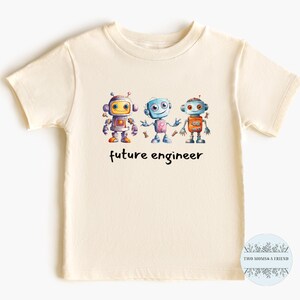 May include: A cream colored t-shirt with a graphic of three robots holding hands. The text "future engineer" is printed below the robots.
