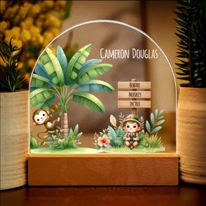 Może przedstawiać: Spersonalizowana lampka nocna z motywem dżungli. Lampka przedstawia chłopca z lornetką, małpę na drzewie i znak z napisem "Uwaga na małpę na drzewie". Lampka jest podświetlona i ma drewnianą podstawę. Na lampce nadrukowano imię "Cameron Douglas".