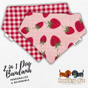 May include: Two reversible dog bandanas. One side features a red and white gingham pattern, the other a pink background with red strawberry illustrations. The bandanas are labeled "2 in 1 Dog Bandana" and "Personalize & Reversible."