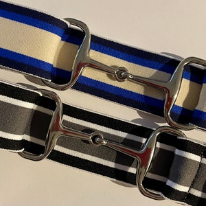 May include: Two striped fabric belts with silver metal buckles. The top belt is navy blue, white and cream. The bottom belt is black, white and grey.