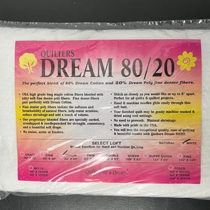 May include: A package of Quilters Dream 80/20 batting, with a pink and white label. The label features text including "Dream 80/20" and product details. The batting is white and comes in various sizes, including Craft, Crib, and King.