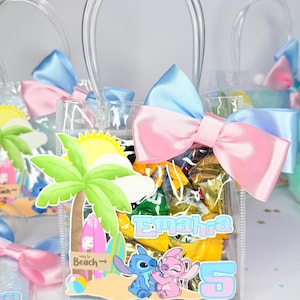 May include: Clear plastic gift bags filled with candy, each adorned with a blue and pink bow. The bags feature a beach-themed graphic with cartoon characters and the name "Emahra" and the number "5".