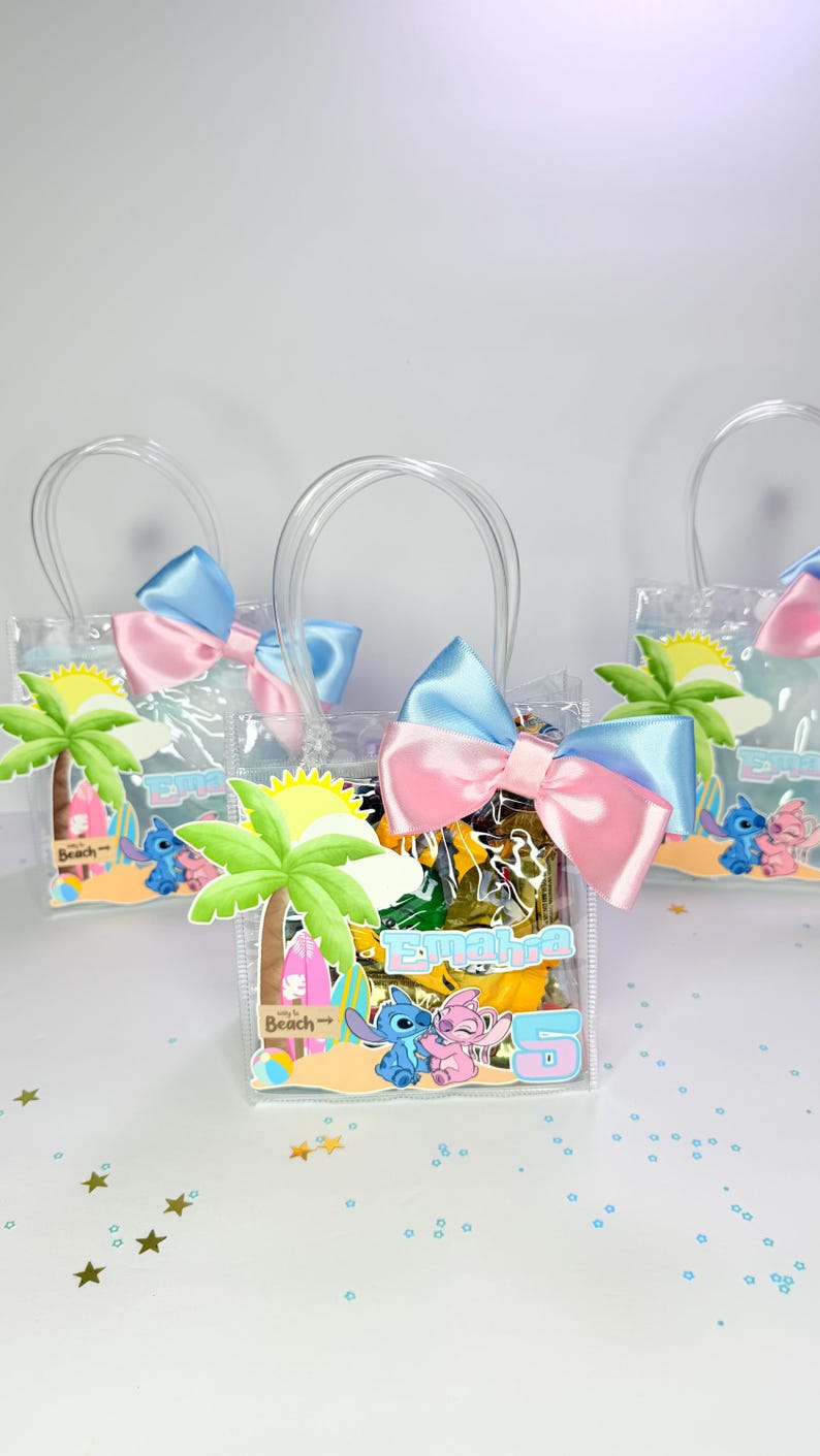 May include: Clear plastic gift bags with blue and pink bows, each featuring a beach-themed design with cartoon characters. The bags have clear handles and are filled with yellow and brown items. The bags have a label with a name and the number 5.