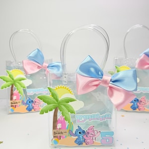 May include: Clear plastic tote bags with blue and pink bows, featuring a beach-themed design with palm trees, cartoon characters, and the name "Emaira" and the number "5". The bags have clear handles.