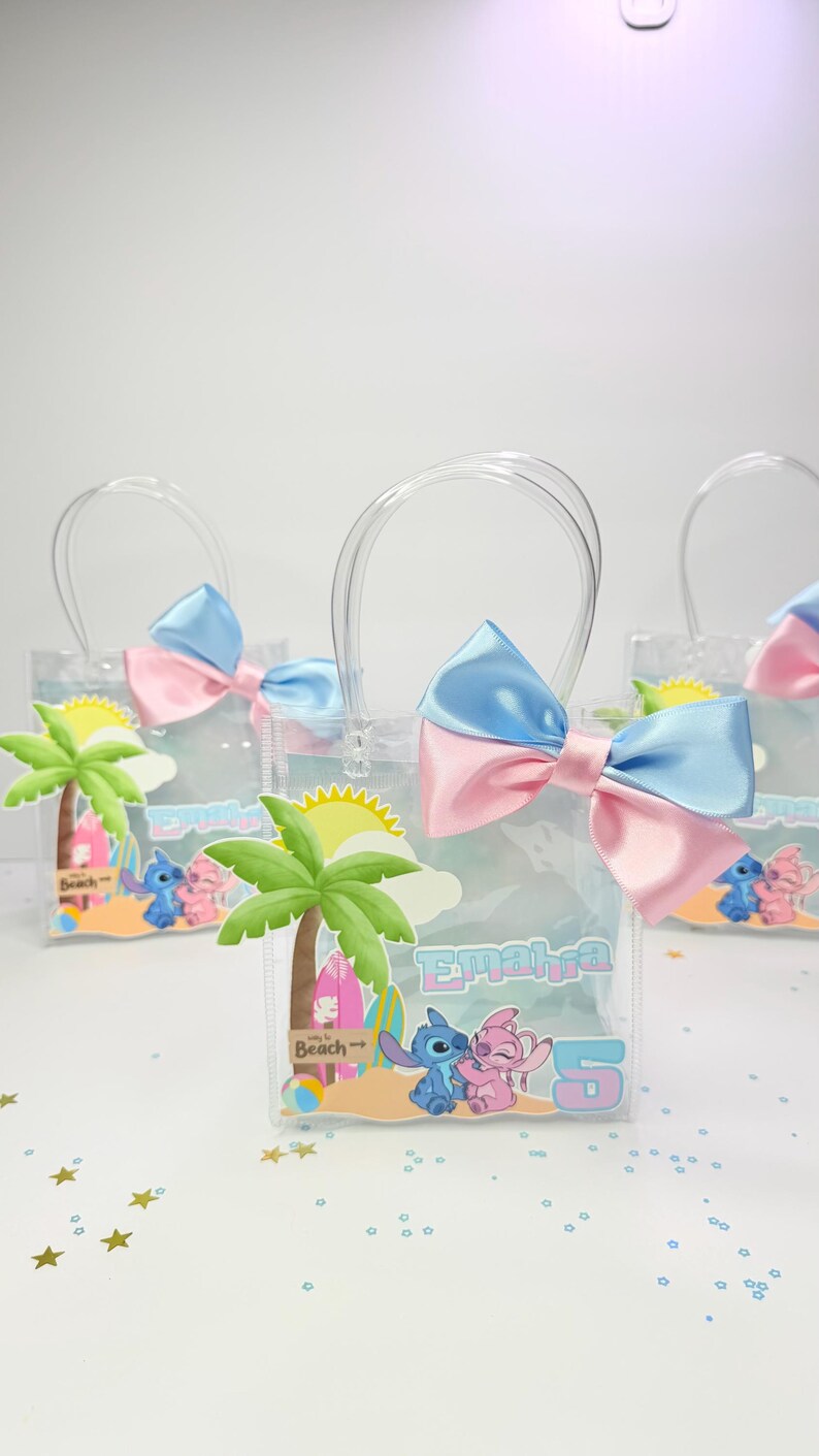 May include: Clear plastic tote bags with blue and pink bows, featuring a beach-themed design with palm trees, cartoon characters, and the name "Emaira" and the number "5". The bags have clear handles.