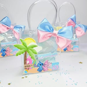 May include: Clear plastic favor bags with blue and pink satin bows. Each bag features a beach-themed graphic with cartoon characters and the name "Emahra" and the number "5". The bags have clear plastic handles.