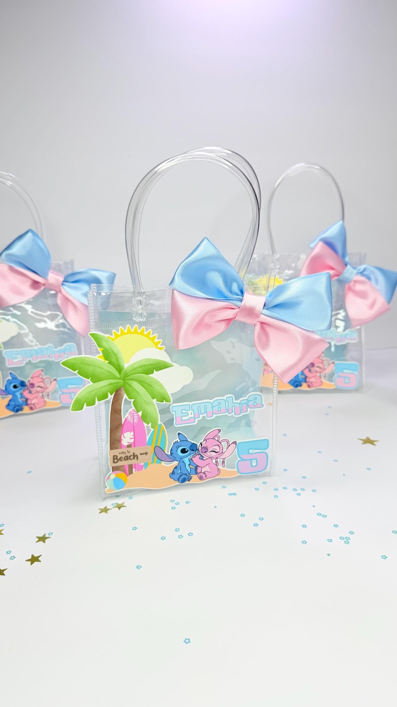 May include: Clear plastic favor bags with blue and pink satin bows. Each bag features a beach-themed graphic with cartoon characters and the name "Emahra" and the number "5". The bags have clear plastic handles.