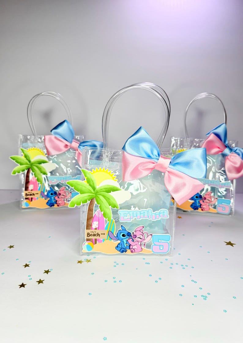 May include: Three clear plastic favor bags with clear handles, each adorned with a blue and pink bow. The bags feature a beach scene with cartoon characters and the name "Emahra" and the number "5".