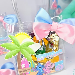 May include: Clear plastic gift bag with a blue and pink bow. The bag features a beach-themed design with a palm tree, sun, and cartoon characters. The bag is filled with wrapped candies and has the name "Emahra" and the number "5" printed on it.