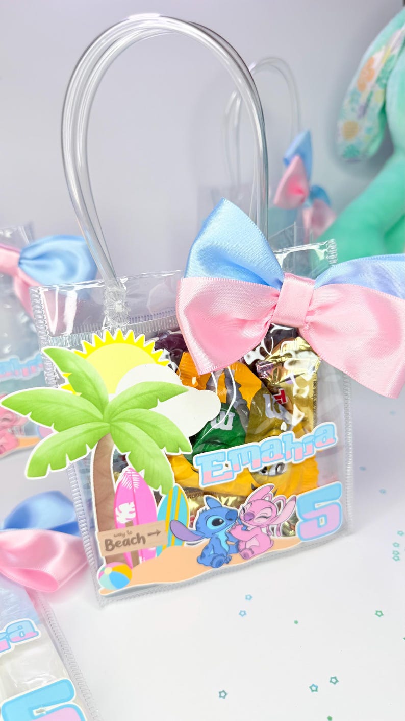May include: Clear plastic gift bag with a blue and pink bow. The bag features a beach-themed design with a palm tree, sun, and cartoon characters. The bag is filled with wrapped candies and has the name "Emahra" and the number "5" printed on it.
