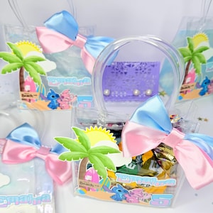May include: Clear plastic favor bags with blue and pink bows, filled with treats. Each bag features a beach-themed graphic with a palm tree, sun, and cartoon characters. The bags have clear handles and the name "Emahra" is printed on them.