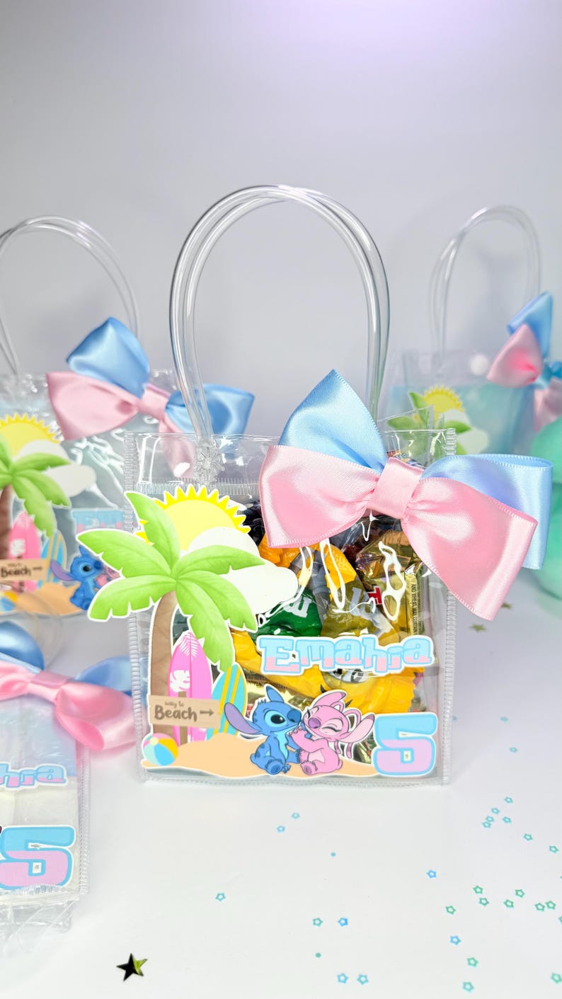 May include: Clear plastic favor bags with blue and pink bows. Each bag features a beach-themed design with cartoon characters and the number 5. The bags have clear handles and are filled with treats.