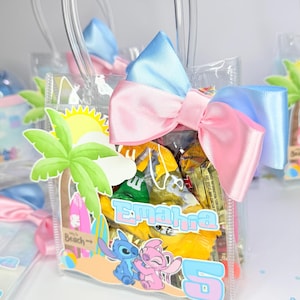 May include: Clear plastic gift bag filled with candy, featuring a beach-themed design with palm trees, surfboards, and the characters Stitch and Angel. The bag is adorned with a pink and blue bow.