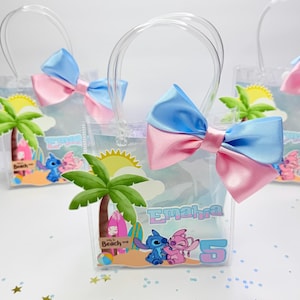 May include: Clear plastic favor bags with blue and pink bows. Each bag features a beach-themed graphic with cartoon characters and the name "Emahia" and the number "5". Palm trees and a sun are also visible.