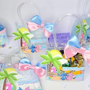 May include: Clear plastic favor bags with blue and pink bows. Each bag features a beach-themed graphic with cartoon characters, a palm tree, and the name "Emaira" with the number "5".