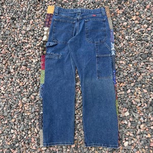 Op de afbeelding: Blauwe denim werkbroek met meerdere zakken en een patchwork ontwerp aan de zijkant. De broek heeft een relaxte pasvorm en een Wrangler label.