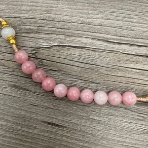 Op de afbeelding: Een roze en witte kralenketting met gouden accenten. De kralen zijn rond en hebben een gladde, gepolijste afwerking.