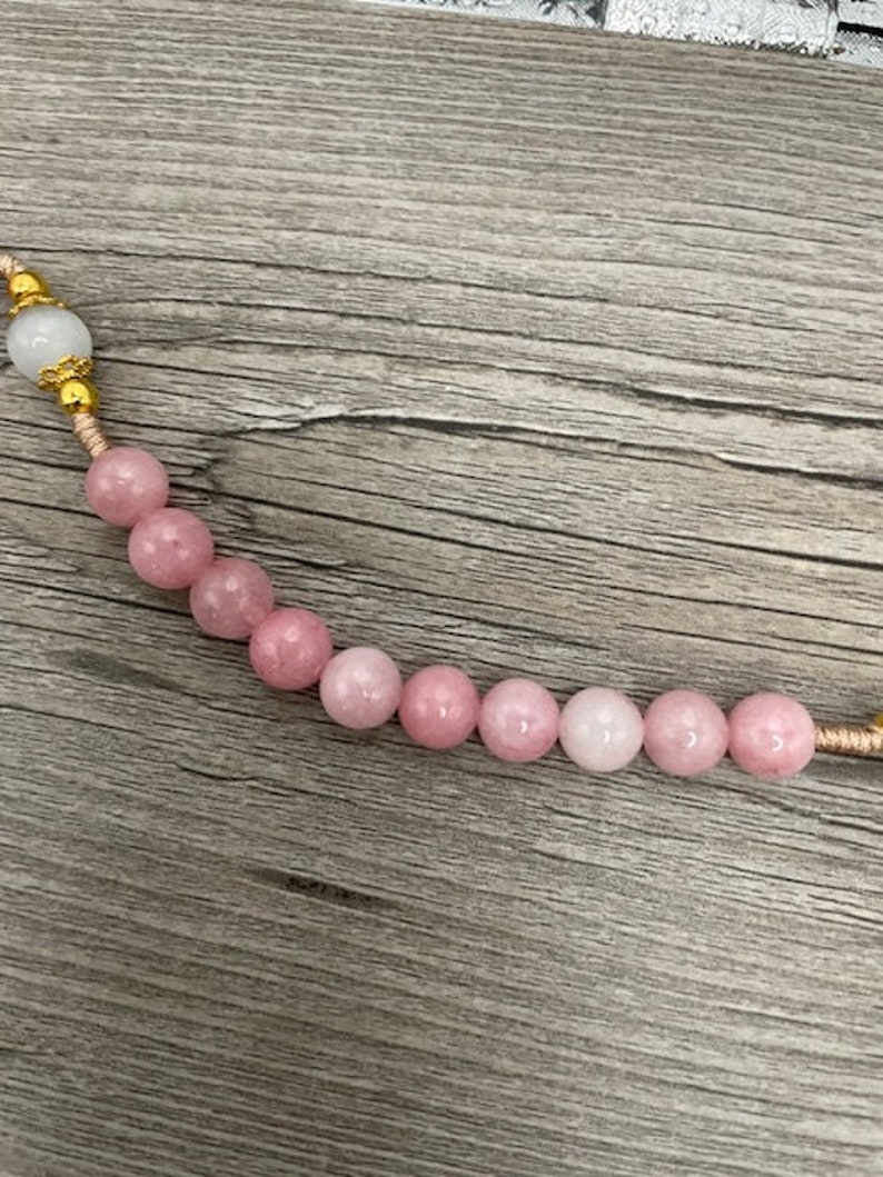 Op de afbeelding: Een roze en witte kralenketting met gouden accenten. De kralen zijn rond en hebben een gladde, gepolijste afwerking.