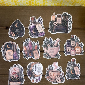 May include: A collection of ten illustrated stickers featuring mystical themes including potion bottles, crystals, tarot cards, a mortar and pestle, a crescent moon, and a teacup, each with various inspirational text phrases printed on them.