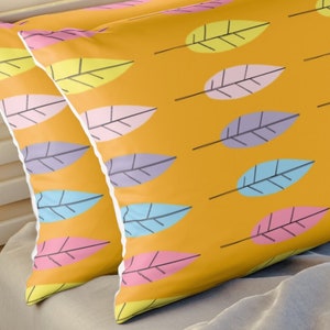 May include: Two yellow pillowcases with a pattern of colorful leaves. The pillowcases are on a bed with a gray blanket.