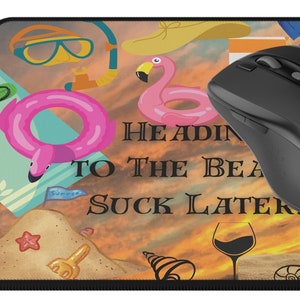Puede incluir: Una alfombrilla de ratón con temática de playa. Presenta una puesta de sol, un flotador de flamenco, una bolsa de playa, una copa de vino y el texto "Heading to the beach, suck later".
