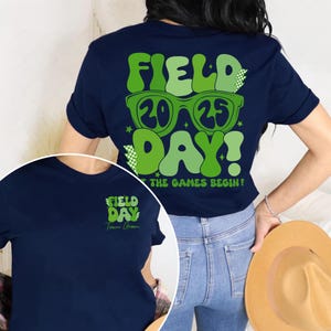 May include: Navy blue t-shirt with a green graphic that says "Field Day 2025" with sunglasses and the text "Let the games begin!" on the back. The front of the shirt has a smaller green graphic that says "Field Day Team Green".