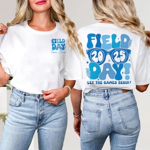 May include: White t-shirt with blue text that says "Field Day" and "Team Blue" on the front. The back of the shirt has blue text that says "Field Day" with a pair of blue sunglasses with the numbers 20 and 25 on the lenses. The text "Let the Games Begin!" is below the sunglasses.