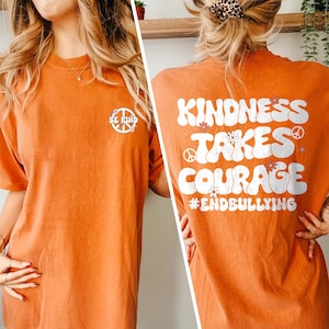 May include: Orange t-shirt with a peace sign and the text "Be Kind" on the front and the text "Kindness Takes Courage #EndBullying" on the back. The text is in a retro, groovy font.