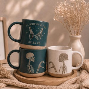 May include: Three ceramic mugs with a speckled base. The top mug is dark green with a skeleton hand pinky promise, the text 'TIL DEATH DO US PART' and '06.25.26'. The bottom two mugs feature skeleton halves forming a heart, one green and one cream.