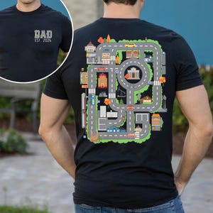 May include: Black t-shirt with a colorful road map design on the back, featuring buildings, trees, and cars. The front of the shirt has the text "DAD EST. 2024" in a green and gray design.