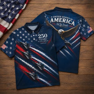 Puede incluir: Un polo azul marino con un dise&ntilde;o patri&oacute;tico. La parte delantera presenta aviones a reacci&oacute;n, rayas rojas y blancas, y el texto "250 YEARS 1776-2026". La parte trasera muestra un &aacute;guila, la bandera estadounidense y el texto "UNITED STATES OF AMERICA 1776-We the People-2026".