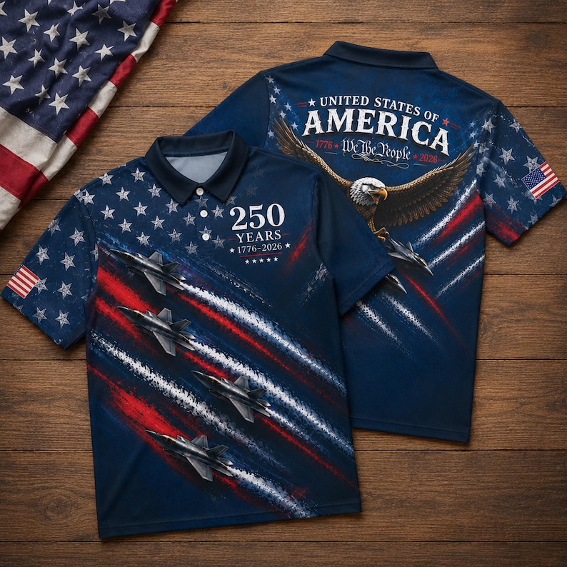 Puede incluir: Un polo azul marino con un dise&ntilde;o patri&oacute;tico. La parte delantera presenta aviones a reacci&oacute;n, rayas rojas y blancas, y el texto "250 YEARS 1776-2026". La parte trasera muestra un &aacute;guila, la bandera estadounidense y el texto "UNITED STATES OF AMERICA 1776-We the People-2026".