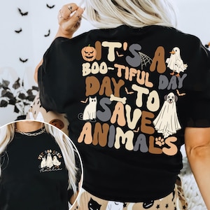 May include: Black t-shirt with the text "It's a Boo-tiful Day to Save Animals" and Halloween-themed graphics. The design includes a pumpkin, spiderweb, ghost, cat, dog, and paw print.