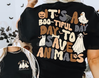 Op de afbeelding: Zwart t-shirt met de tekst "It's a Boo-tiful Day to Save Animals" en Halloween-thema graphics. Het ontwerp bevat een pompoen, spinnenweb, spook, kat, hond en een pootafdruk.