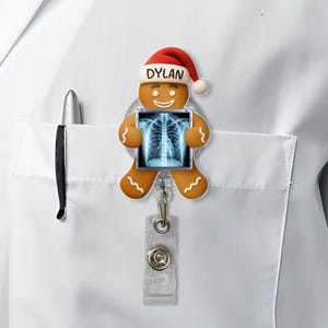 May include: A gingerbread man badge reel with a Santa hat that says "Dylan". The gingerbread man is holding a blue and white X-ray image. The badge reel is attached to a clear plastic clip.