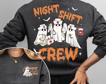 May include: A dark gray sweatshirt with the text "Night Shift Crew" in orange and black. The design features three ghosts dressed as nurses with medical supplies. The sweatshirt has a small pocket on the left side with a smaller version of the design.