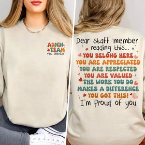 May include: A beige sweatshirt with the text "ADMIN TEAM Mrs. Wachter" on the front. The back of the sweatshirt has the text "Dear staff member reading this... YOU BELONG HERE YOU ARE APPRECIATED YOU ARE RESPECTED YOU ARE VALUED THE WORK YOU DO MAKES A DIFFERENCE YOU GOT THIS! I'm proud of you" in a colorful retro font.