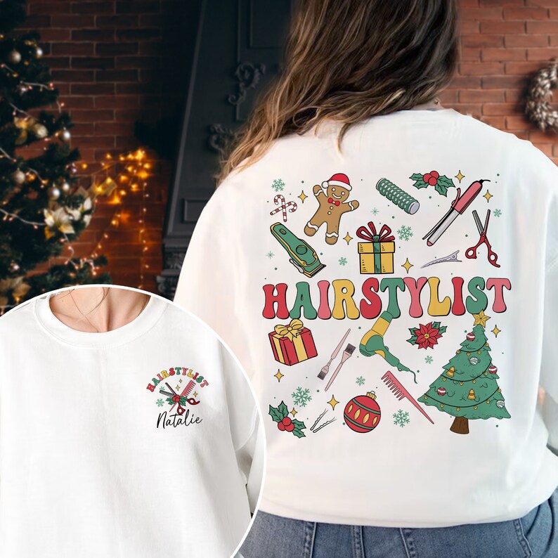 Op de afbeelding: Witte trui met een kerstthema met een peperkoekman, een kerstboom en de tekst "HAIRSTYLIST". De trui heeft ook een klein zakje aan de voorkant met de tekst "HAIRSTYLIST Natalie".