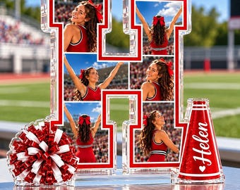 Op de afbeelding: Een doorzichtige acryl fotolijst in de vorm van een H met vijf afzonderlijke foto's van een cheerleader in een rood uniform. Links staat een rood-witte pompon en rechts een rode glitter-megafoon met de naam Helen in het wit gedrukt.