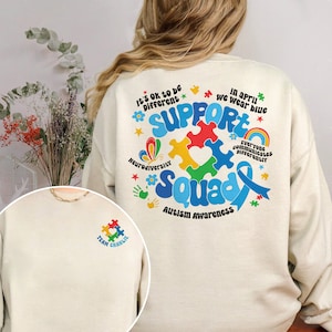 May include: A cream-colored sweatshirt with a blue ribbon, puzzle pieces, and the text "Support Squad" in rainbow colors. The text "It's Ok to be Different" and "Neurodiversity" are also included. The back of the sweatshirt has a small pocket with a puzzle piece and the text "Team Charlie".