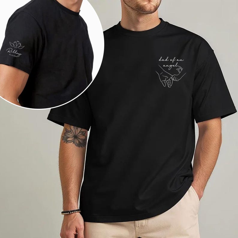 May include: Black t-shirt with the text "dad of an angel" and a line drawing of two hands holding each other. The left sleeve has a small floral design and the name "Riley" printed on it.