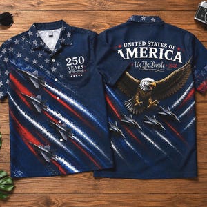 Puede incluir: Una camisa azul marino con botones y un dise&ntilde;o patri&oacute;tico. La camisa presenta estrellas blancas sobre un fondo azul, aviones y rayas rojas y blancas. La parte trasera de la camisa muestra un &aacute;guila, la bandera estadounidense y el texto "United States of America".