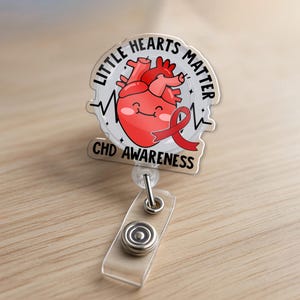 May include: A clear, heart-shaped badge reel with the text "Little Hearts Matter" and "CHD Awareness." The design features a smiling red heart with a red ribbon. The reel has a clear plastic strap and a metal clip.