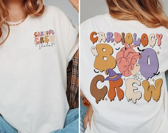 Puede incluir: Camiseta blanca con un estampado gráfico del texto "Cardiology Boo Crew" en letras que gotean con un corazón, fantasmas y un sombrero de bruja. El texto "Violet" está impreso en la parte delantera de la camiseta.